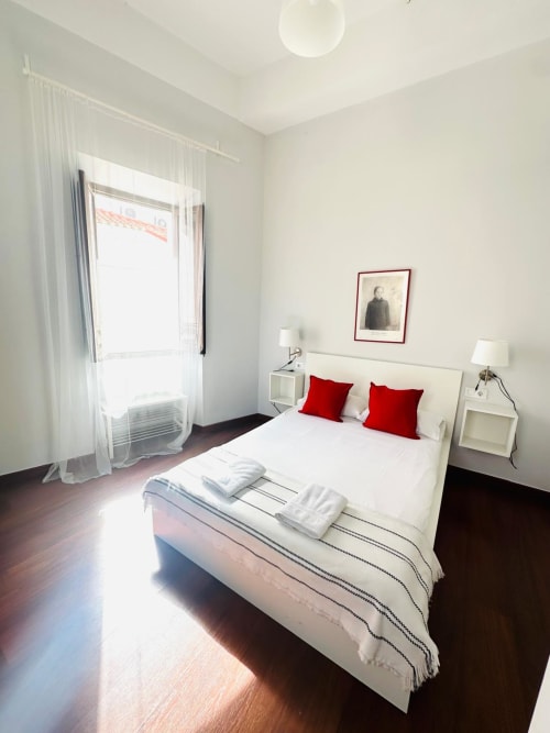Habitación luminosa del apartamento Gestyp-AT en Mérida con cama blanca, almohadas rojas, piso de madera oscura y luz natural