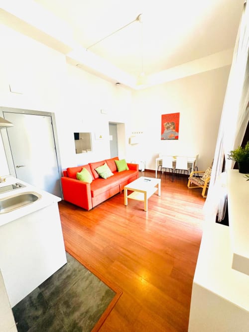 Luminosa sala de estar en Mérida con sofá rojo, pisos de madera, cocina integrada y muebles modernos