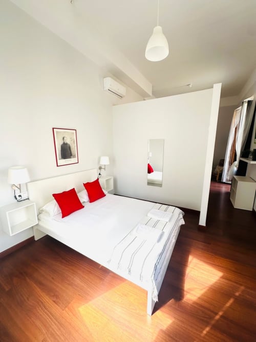 Dormitorio moderno del apartamento Gestyp-AT en Mérida con cama blanca, almohadas rojas y pisos de madera