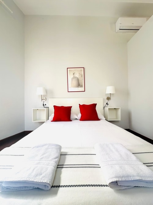 Habitación moderna del apartamento Gestyp-AT en Mérida con cama blanca, almohadas rojas, lámparas de pared y decoración minimalista