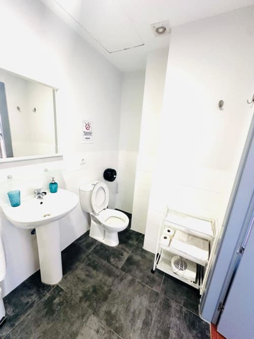 Baño moderno del apartamento Gestyp-AT en Mérida con accesorios blancos, piso de azulejos oscuros y lavamanos de pedestal