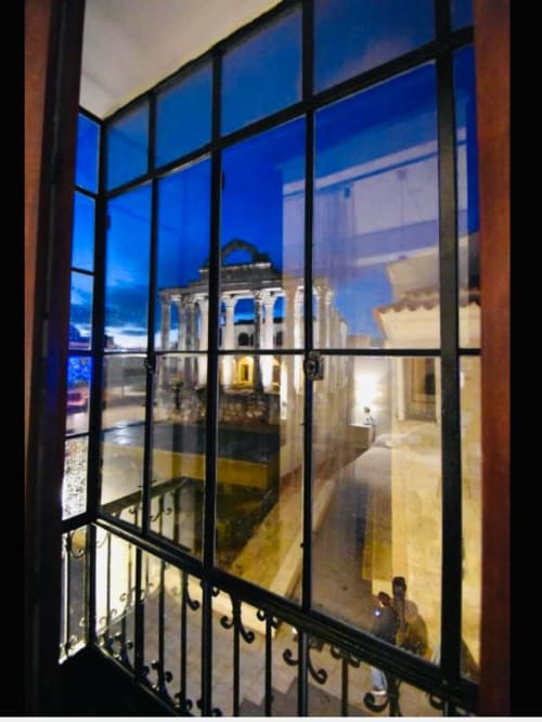 Vista desde el apartamento Gestyp-AT en Mérida a través de ventana enrejada al atardecer, con arquitectura colonial iluminada