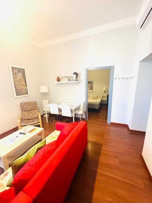 Moderno salón con sofá rojo, zona de comedor y vista al dormitorio en Mérida, España