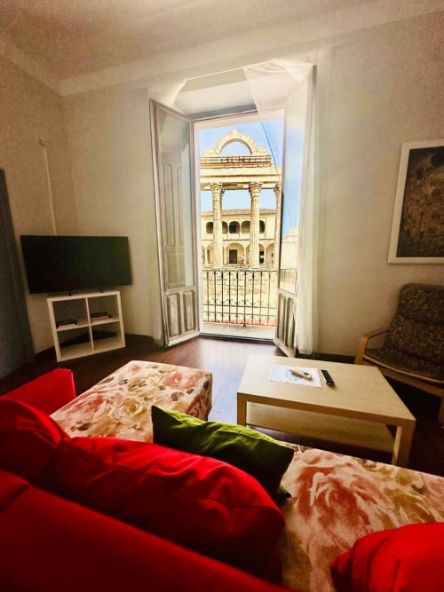 Sala de estar moderna en Mérida con sofá rojo, escritorio de madera y balcón con vista a edificio histórico