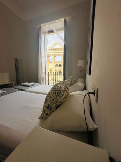 Dormitorio de apartamento en Mérida con camas gemelas con vistas a la arquitectura dorada histórica a través de puertas de balcón