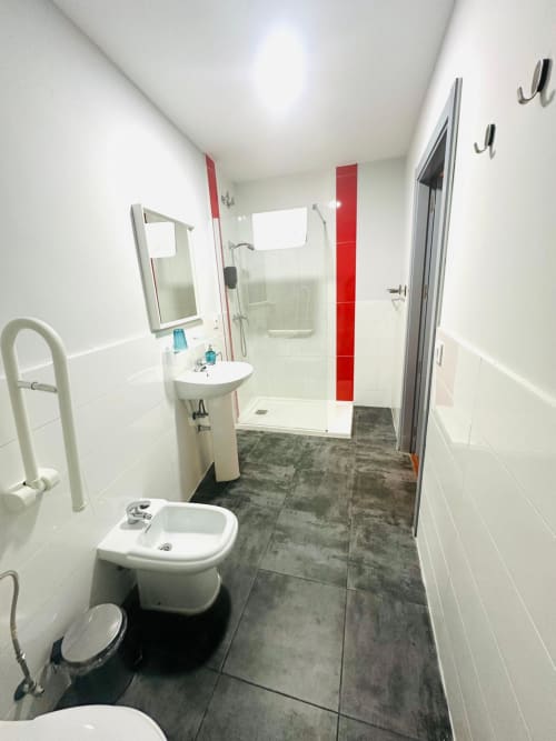 Baño moderno en departamento de Mérida con azulejos blancos, detalles rojos, ducha tipo walk-in, lavamanos de pedestal y pisos de azulejos oscuros