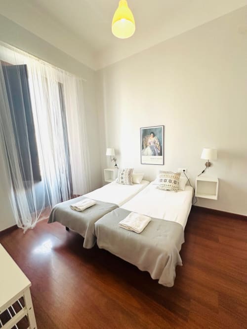 Apartamento con dormitorio doble en Mérida, pisos de madera, ropa de cama blanca, obras de arte y luz natural desde ventana con cortinas