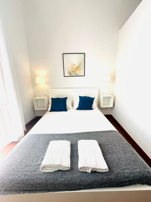 Moderno dormitorio en Mérida con cabecera blanca, almohadas azules, colcha gris y toallas a juego.