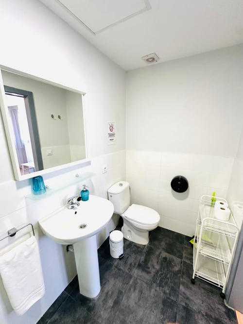 Baño moderno del apartamento Gestyp-AT en Mérida con lavamanos blanco, inodoro, baldosas oscuras y espejo de pared