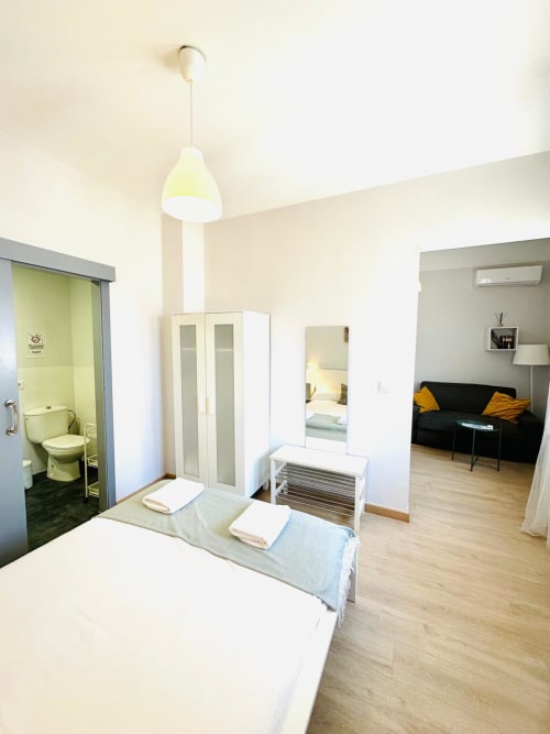 Moderno dormitorio de apartamento en Mérida con cama, armario, baño ensuite, lámpara colgante y sala de estar con sofá negro