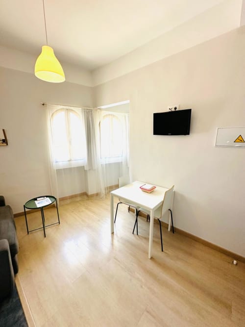 Sala de estar moderna en Mérida con mesa blanca, sillas negras, lámpara colgante amarilla, TV y luz natural