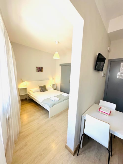Apartamento moderno en Mérida con dormitorio, cama blanca, lámpara colgante, suelo de madera y zona de trabajo