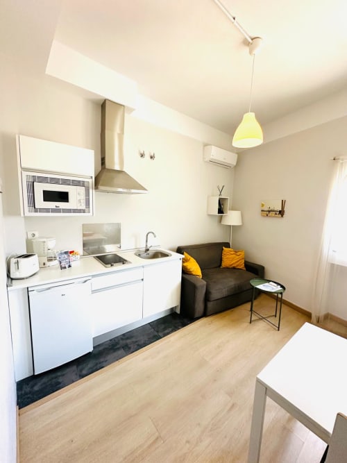 Cocina y sala de estar modernas en Mérida con muebles blancos, encimera negra y asientos cómodos