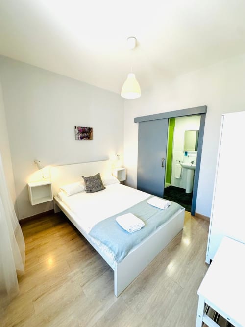 Moderno dormitorio en Mérida con cama blanca, baño en suite, lámpara colgante y pisos de madera.