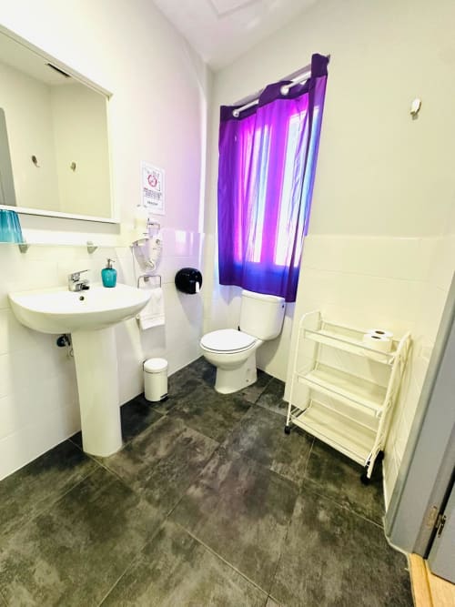 Baño moderno en apartamento de Mérida con accesorios blancos, piso de azulejos oscuros y cortina de ducha morada