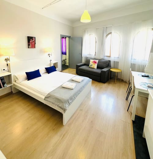Moderno estudio en Mérida con cama, sofá y vistas a la ciudad a través de grandes ventanales