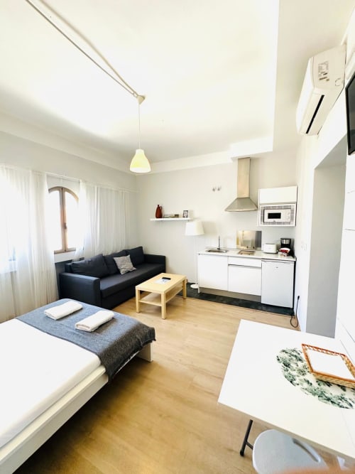 Moderno estudio en Mérida con cama, sofá negro, cocineta y pisos de madera