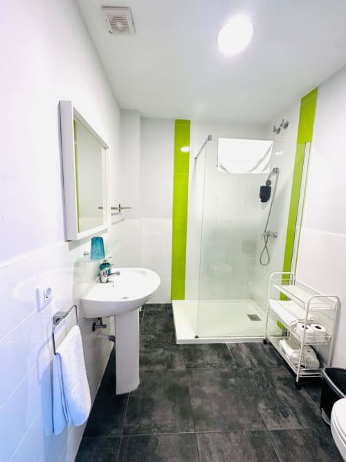 Baño moderno en apartamento de Mérida con azulejos blancos, detalles verde lima, ducha tipo walk-in y piso oscuro.