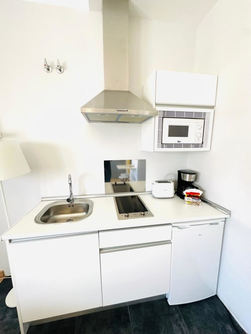 Cocina moderna y compacta en apartamento de Mérida con gabinetes blancos, fregadero de acero inoxidable, estufa y microondas