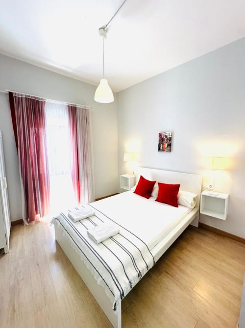 Dormitorio moderno en apartamento Gestyp-AT de Mérida con cama blanca, almohadas rojas y cortinas burdeos