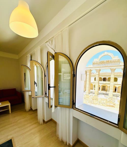 Apartamento en Mérida con ventanas arqueadas con vistas a ruinas romanas, columnas, puertas de madera, cortinas crema y lámpara de techo