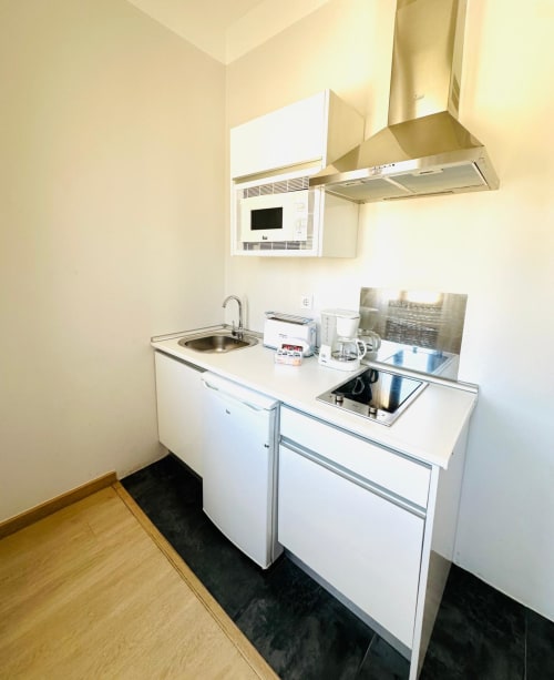 Cocina moderna y compacta en apartamento de Mérida con gabinetes blancos, microondas, estufa y electrodomésticos de acero inoxidable