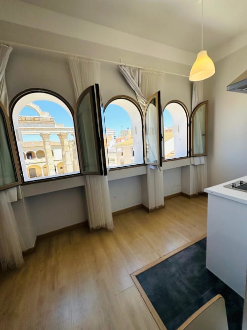 Apartamento luminoso en Mérida con ventanas arqueadas que dan a la arquitectura colonial española histórica y cielo azul despejado