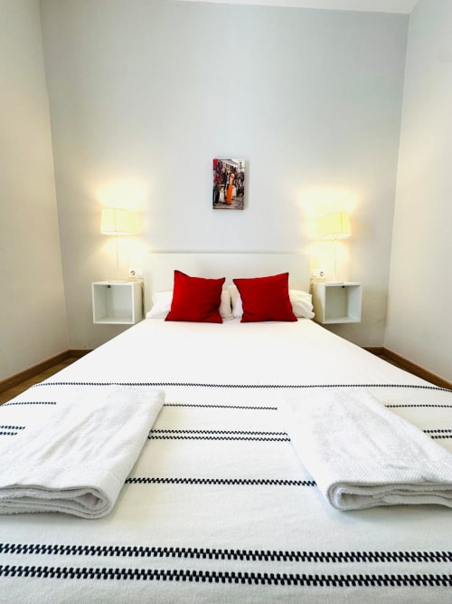 Dormitorio moderno en apartamento de Mérida con almohadas rojas, sábanas blancas, lámparas gemelas y decoración minimalista