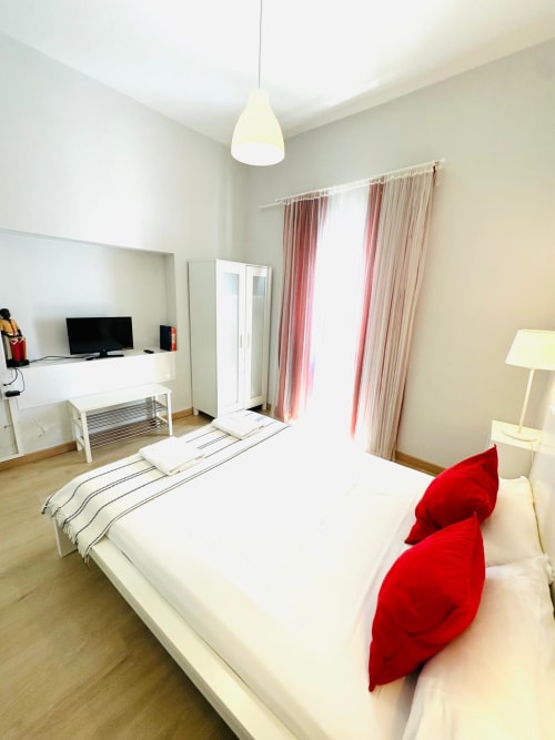 Dormitorio moderno en apartamento Gestyp-AT en Mérida con cama blanca, almohadas rojas, lámpara colgante y cortinas rosas