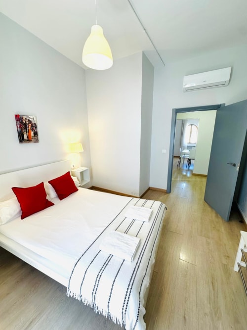Moderno dormitorio en departamento de Mérida con cama blanca, almohadas rojas, lámpara colgante y piso de madera