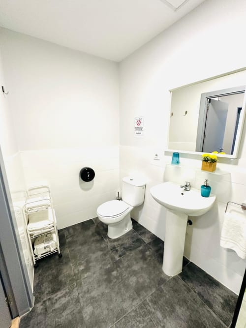 Baño moderno y limpio en apartamento Gestyp-AT en Mérida con sanitarios blancos, lavamanos de pedestal y pisos de azulejos oscuros