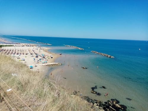 Vista aérea de playa de arena con aguas turquesas, rompeolas rocoso y bañistas cerca de Crecchio, Italia