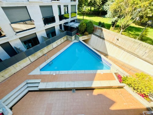Vista aérea de la piscina de Holibai en Baiona con terraza, edificio de apartamentos moderno y jardines exuberantes