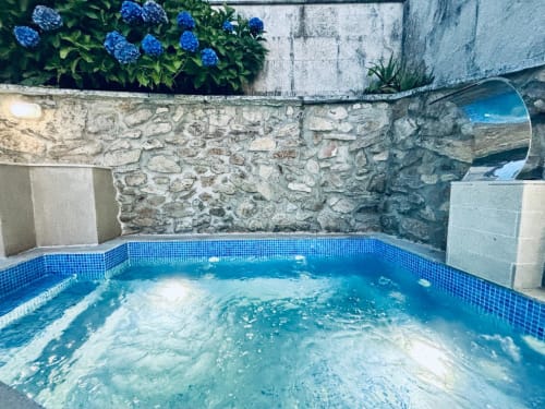 Piscina climatizada al aire libre con borde de azulejos azules en la villa Vila Natercia de Baiona, con muro de piedra de fondo