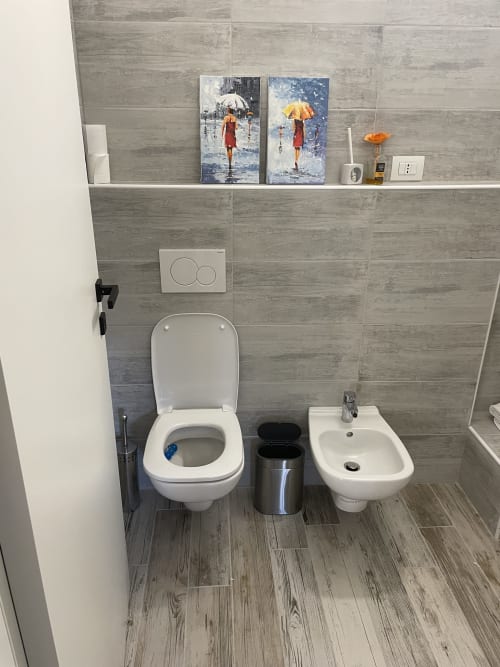 Bagno moderno dell'appartamento Varenna by Foot con toilette, bidet, lavabo e mensola decorativa con quadri di ombrelli