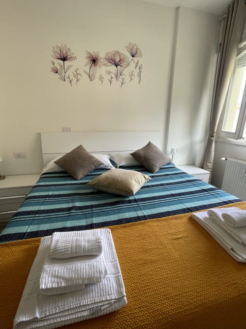 Camera luminosa a Varenna by Foot con letto a righe blu, decorazioni floreali sulla parete e asciugamani bianchi freschi sul giallo