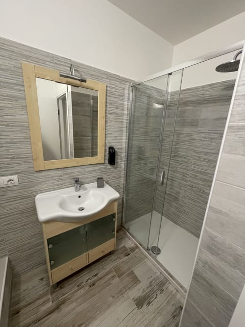 Bagno moderno nell'appartamento di Varenna con piastrelle grigie, mobile in legno, lavandino bianco e box doccia in vetro