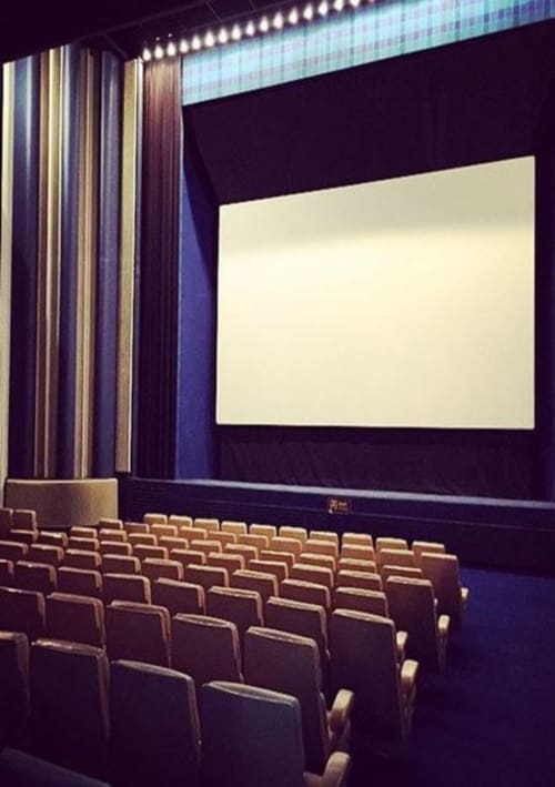 Salle de cinéma vide aux rangées de fauteuils rouges, grand écran de projection et rideaux à rayures au Fassardy de Châteauroux