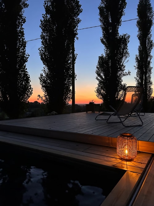 Vue du coucher de soleil depuis la terrasse du Domaine de Blanvatel avec peupliers, chaises longues et lanterne lumineuse à Saint-Pierre-en-Auge