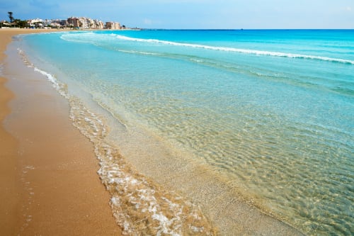 Aguas turquesas cristalinas y playa de arena dorada en Burriana con edificios costeros al fondo