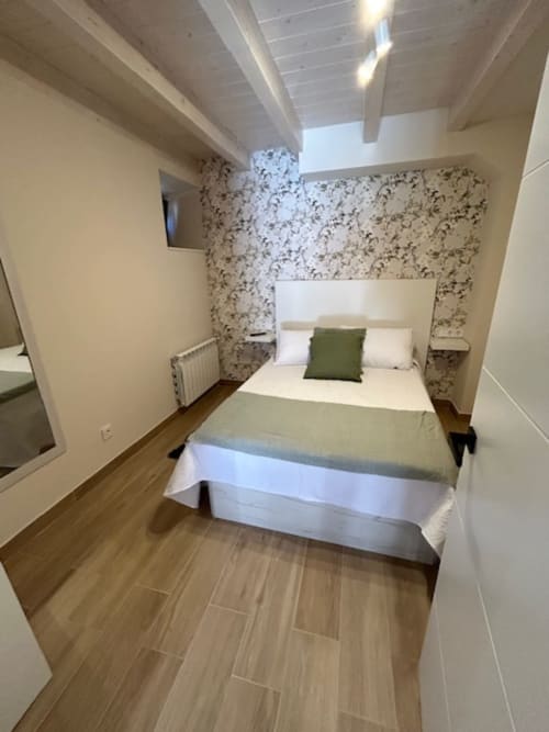 Acogedor dormitorio de apartamento en Las Llaviadas con papel tapiz floral, suelos de madera y vistas a la montaña desde Ortiguero de Cabrales