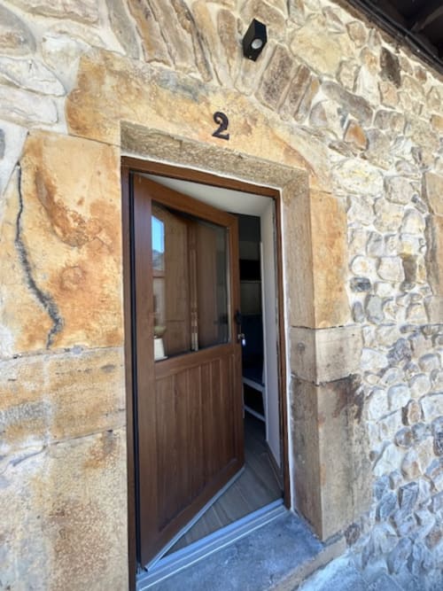 Puerta de madera de entrada al apartamento Las Llaviadas en Ortiguero de Cabrales con fachada de piedra