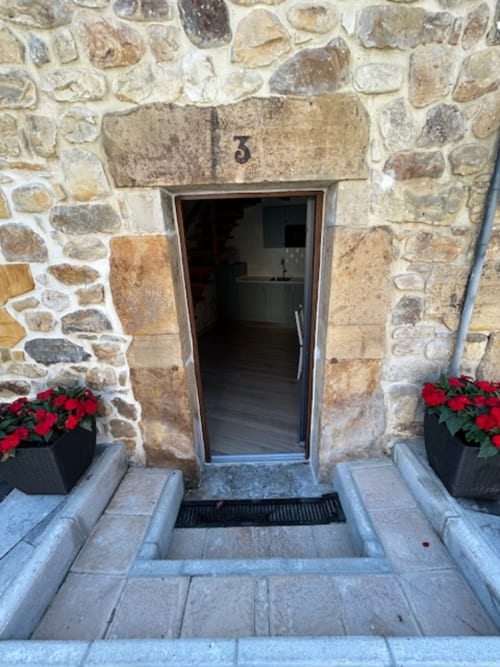 Entrada del apartamento en Las Llaviadas, Ortiguero de Cabrales, con fachada de piedra y flores rojas