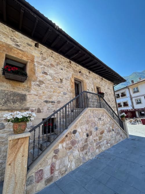 Entrada de edificio de piedra con escalera de barandilla metálica en el hotel Las Llaviadas de Ortiguero de Cabrales, España