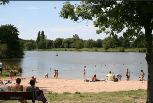 Plage de sable au lac de Châteauroux avec baigneurs, arbres et ciel dégagé - Gîte Le Fassardy à proximité