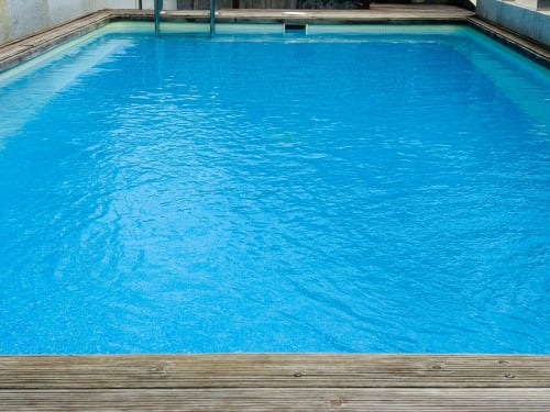Piscina azul brillante en el apartamento Holibai de Baiona con terraza de madera y barandillas metálicas