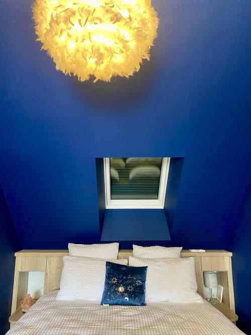 Chambre aux Chambres d'hôtes Lady Jule avec murs bleus, lit en bois, luminaire plume et fenêtre de toit