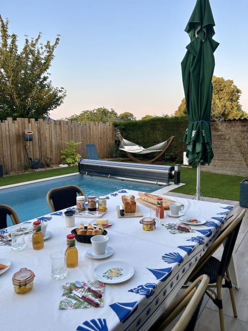 Table du petit-déjeuner au bord de la piscine de Lady Jule B&B à Sainte-Luce-sur-Loire avec viennoiseries, café et vue sur le hamac