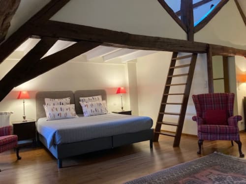 Spacious attic bedroom at Le Fassardy B&B in Châteauroux with beamed ceilings, queen bed, burgundy armchair, and wooden