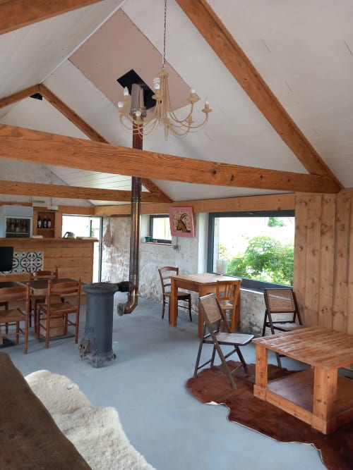Intérieur rustique ouvert à La Maison De Fleurat à Domeyrot avec poutres apparentes, lustre, tables de salle à manger et pierre